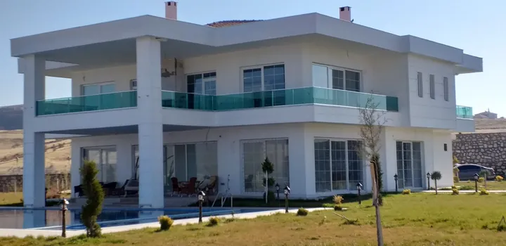 Bahçeli, geniş cam yüzeyli ve cam balkon korkuluklu iki katlı beyaz villa